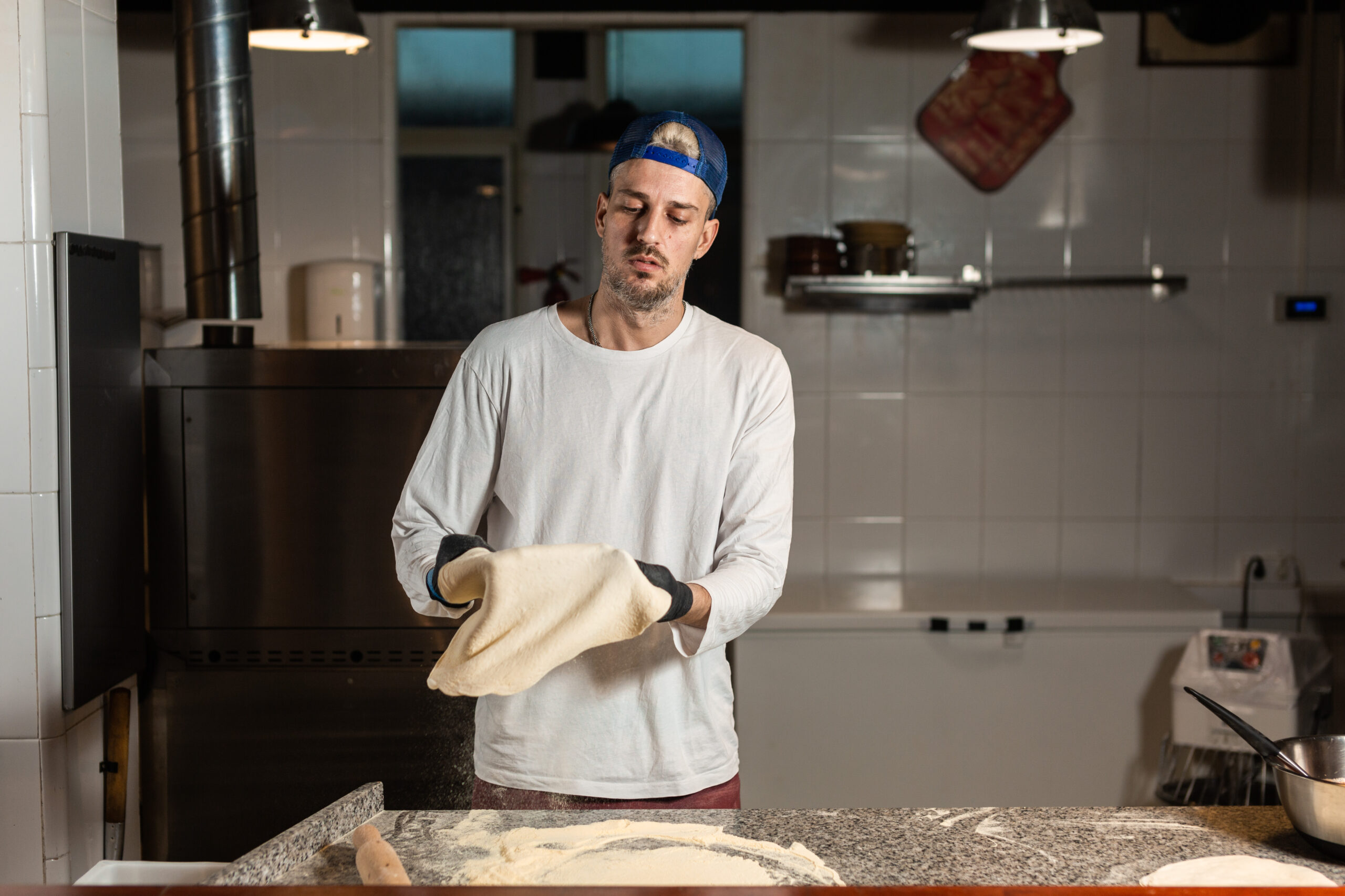 pizza boy in cap and gloves kneads pizza dough in the kitchen of a pizzeria restaurant